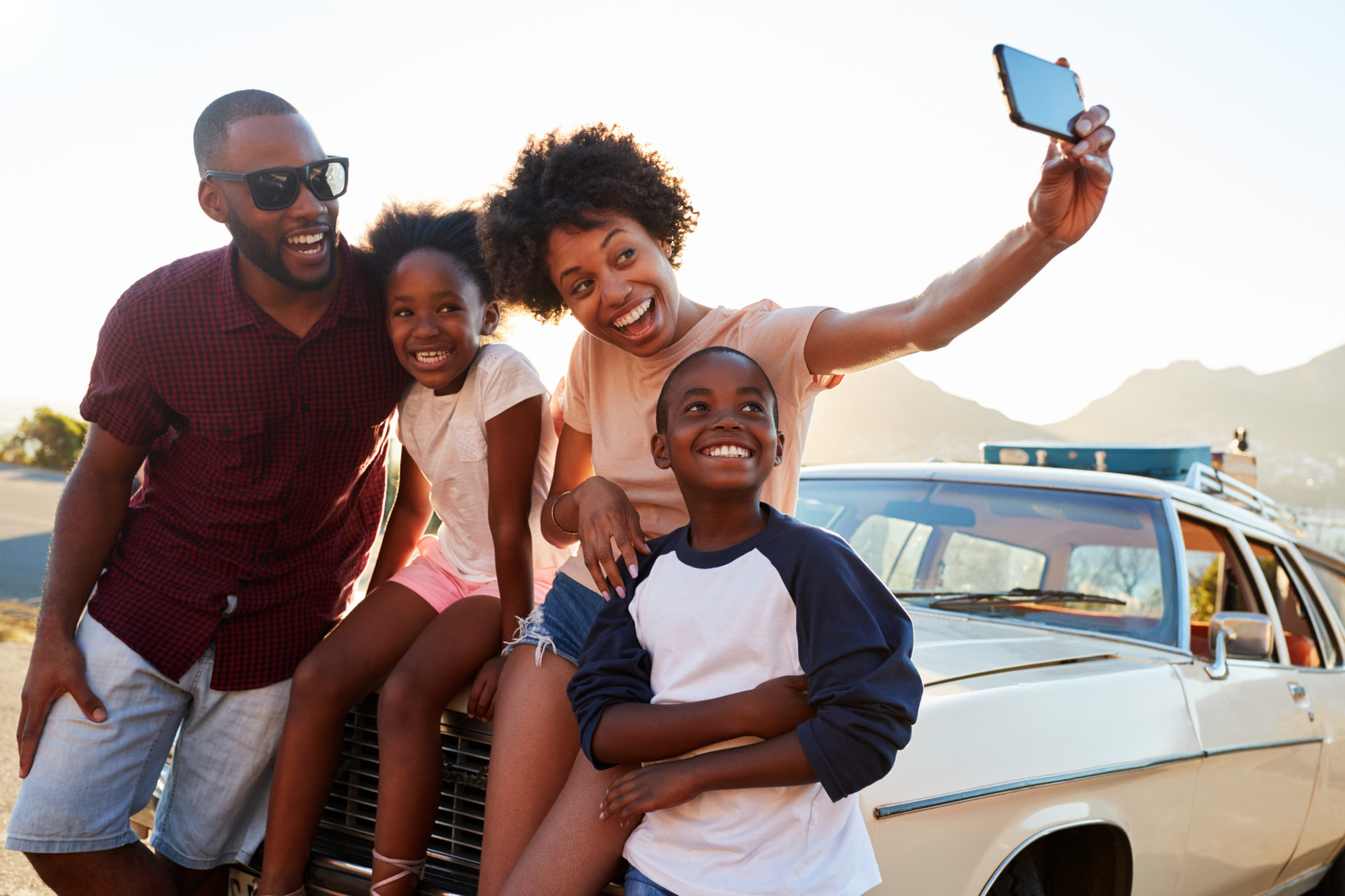 Famille heureuse prenant des autoportraits sur le capot d’une voiture.