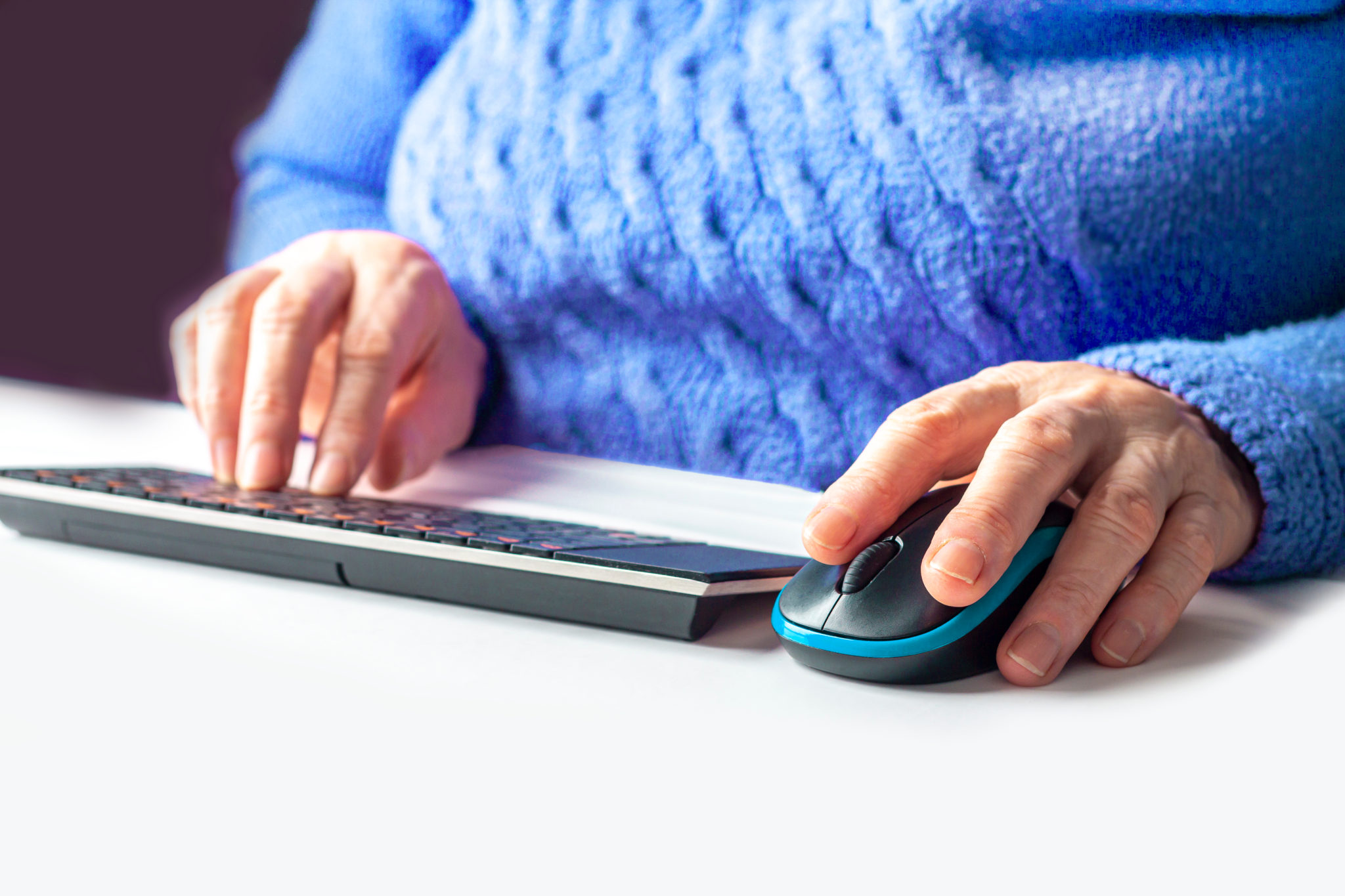 Gros plan des mains d’une personne âgée qui utilise une souris et un clavier.