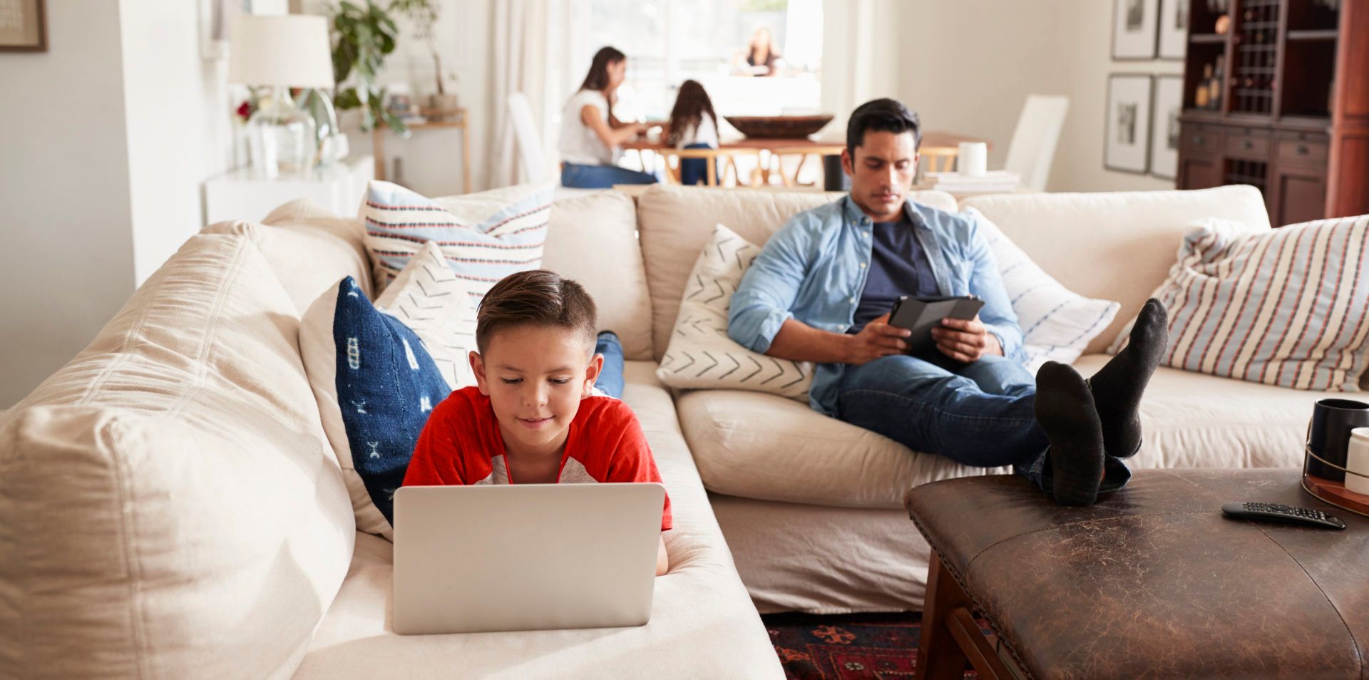Enfant qui utilise un ordinateur portable sur un canapé pendant qu’une personne adulte regarde une tablette.