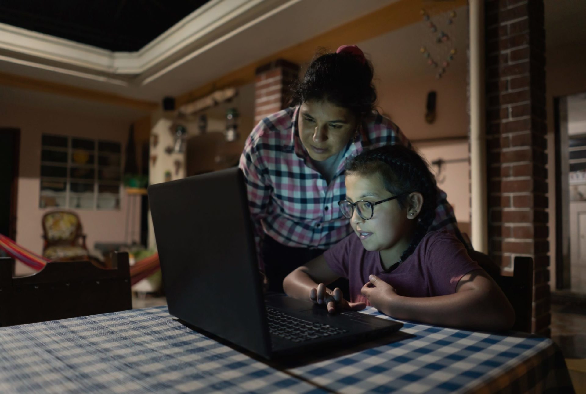 Adulte et enfant utilisant un ordinateur portable pour faire les devoirs dans une salle à manger.
