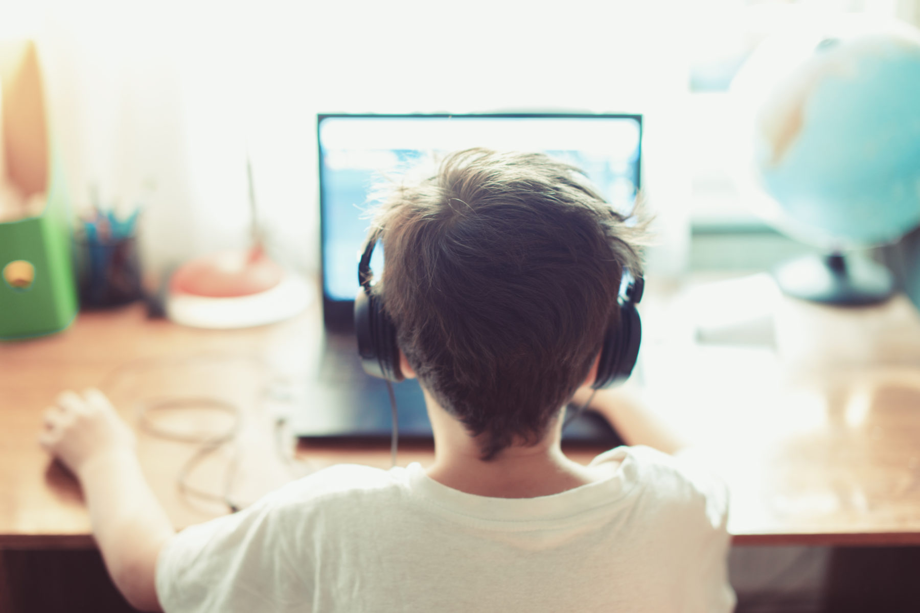 Gros plan de l’arrière de la tête d’un enfant qui utilise un ordinateur portable et porte des écouteurs à un bureau à la maison.