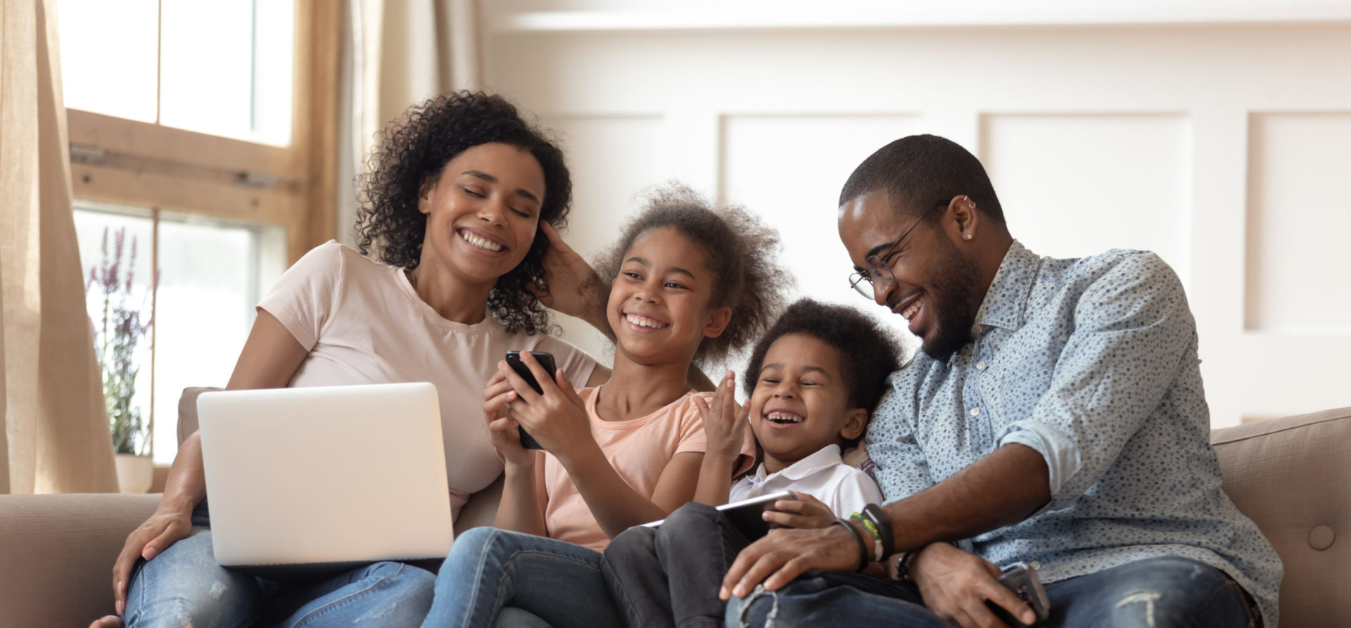 Famille heureuse sur un canapé qui utilise un ordinateur portable, une tablette et un téléphone intelligent.